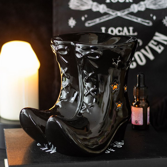 Black boot-shaped vase with a candle and bottle on a dark surface