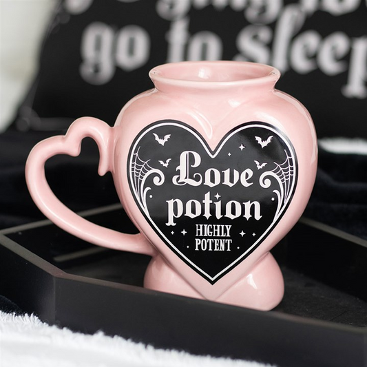 Pink mug with heart-shaped handle and 'Love potion Highly Potent' design on a black background.