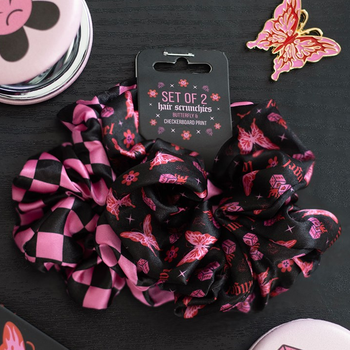 Set of 2 black and pink patterned scrunchies with packaging on a dark surface.