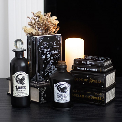 Decorative set with black bottles labeled 'Dried Gravestones' and 'Wards & Wonders', surrounded by books and a candle.