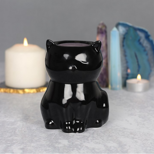 Black cat-shaped candle holder on a gray surface with candles and crystals in the background.