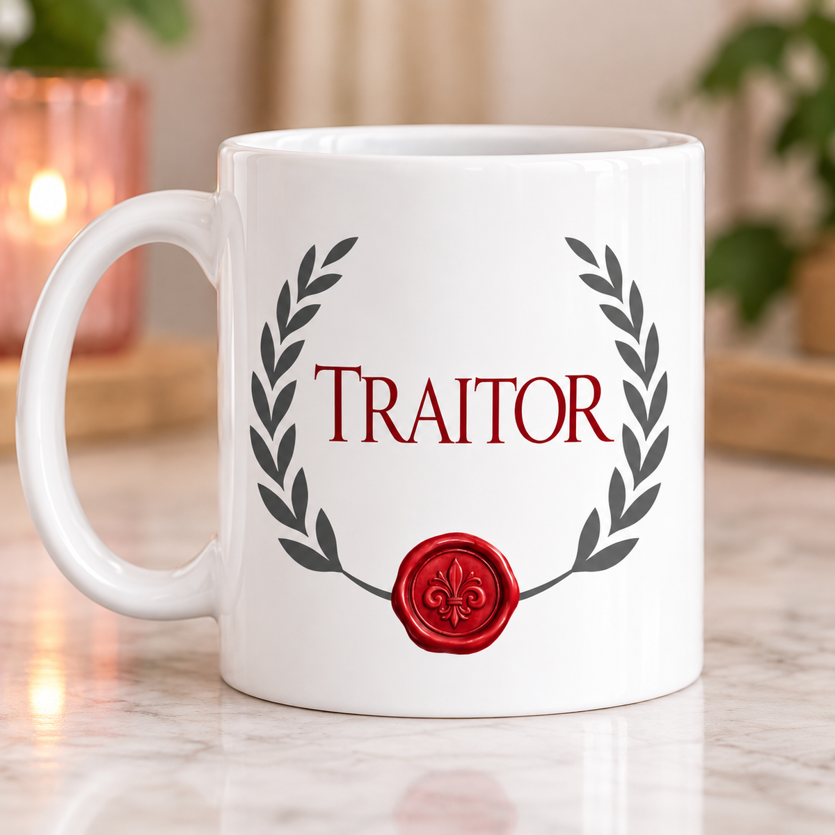 A white ceramic mug with a red wax seal and the word 'TRAITOR' in red serif lettering, framed by a dark gray laurel wreath. The mug is set on a light marble surface with a softly blurred background containing a warm lit candle and green plants.