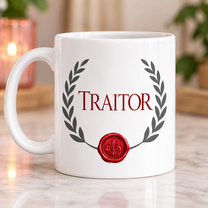A white ceramic mug with a red wax seal and the word 'TRAITOR' in red serif lettering, framed by a dark gray laurel wreath. The mug is set on a light marble surface with a softly blurred background containing a warm lit candle and green plants.