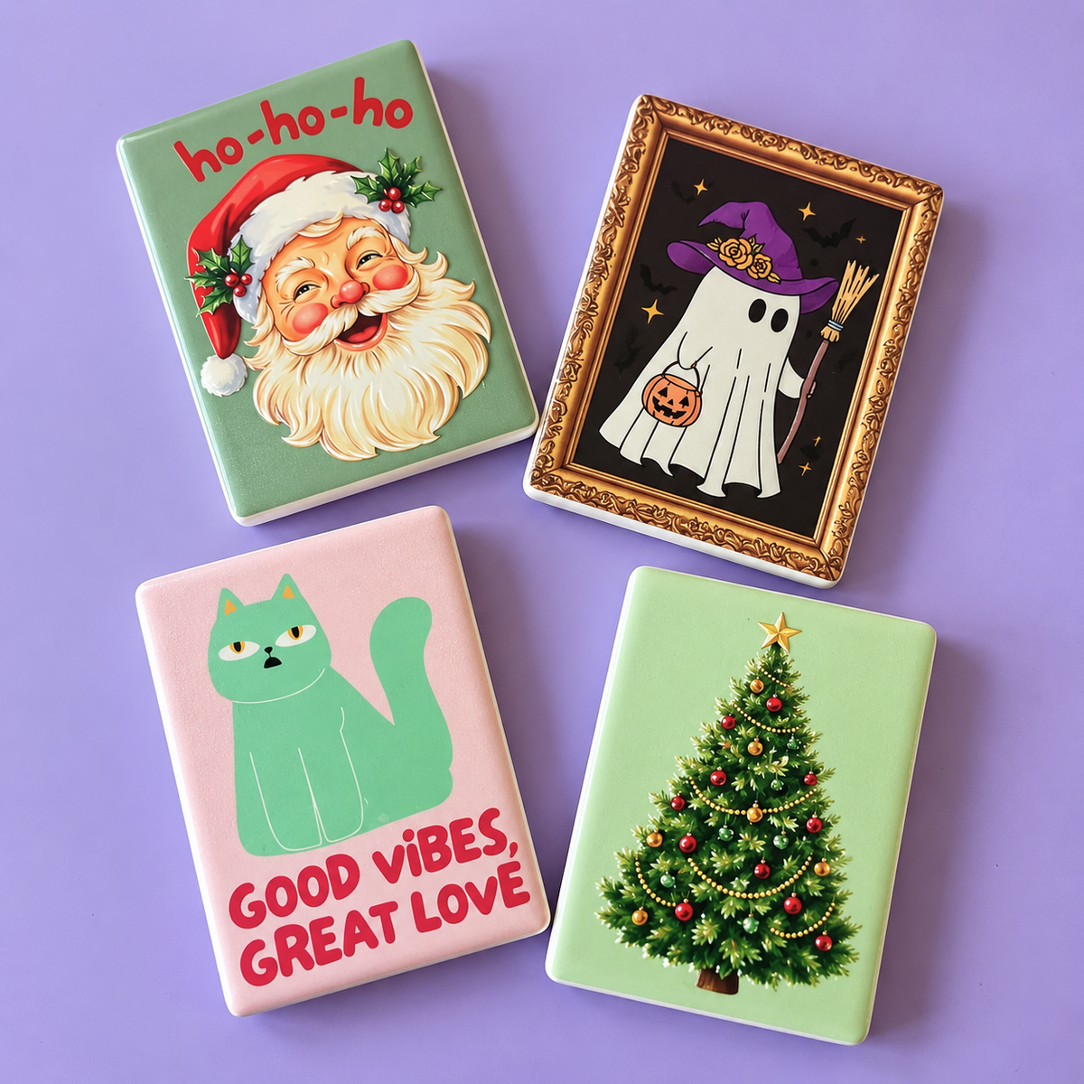 Four rectangular decorative magnets with rounded corners arranged in a square on a lavender background. Each item features a different Halloween-themed illustration: Santa with the text 'ho-ho-ho', a framed ghost in a witch hat, a green cat with the text 'GOOD VIBES, GREAT LOVE', and a decorated Christmas tree.