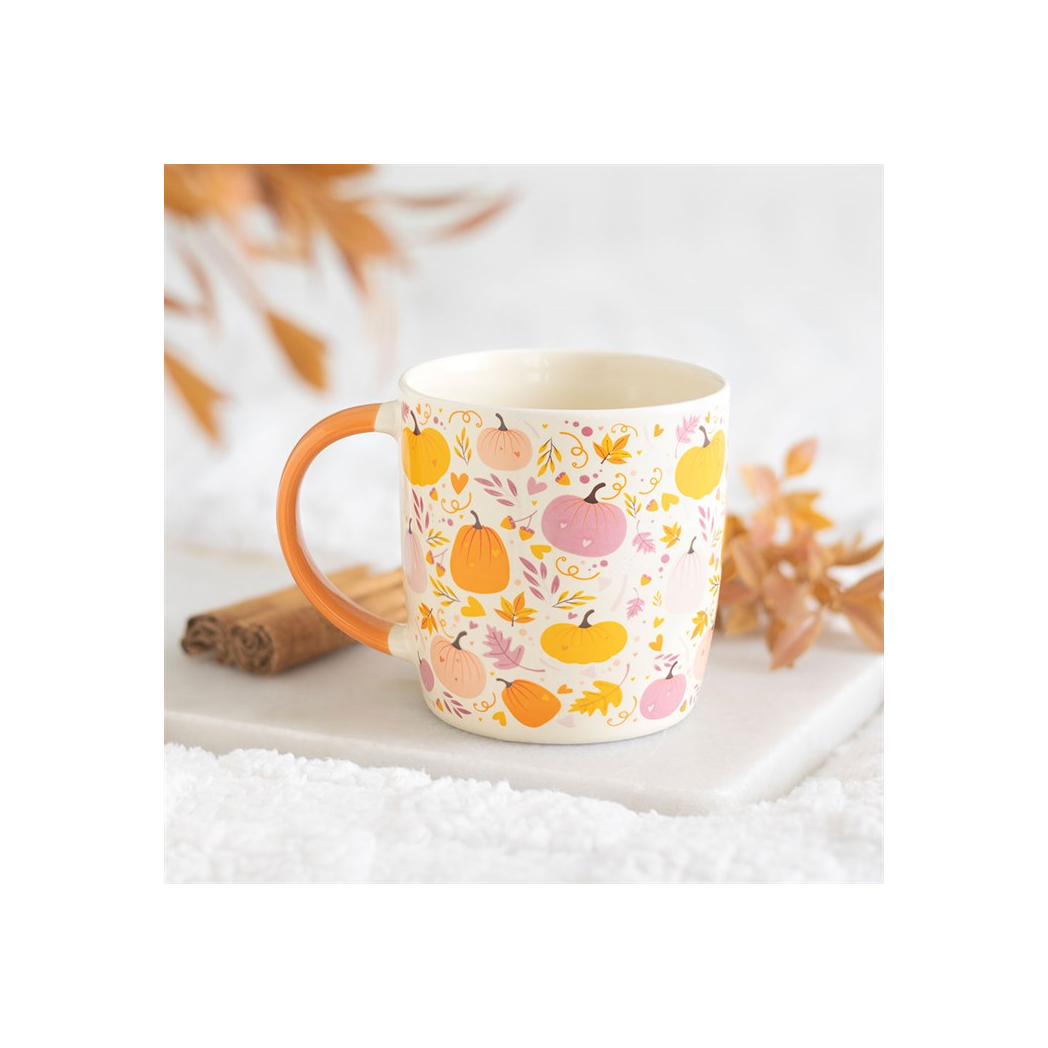 Mug with autumn-themed design featuring pumpkins and leaves on a white surface.