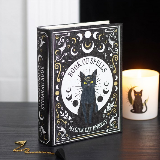 Decorative book titled 'Book of Spells: Magick Cat Energy' with a black cat illustration on a wooden surface.