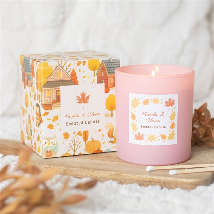 Pink scented candle with a decorative box featuring autumn-themed illustrations on a wooden surface.